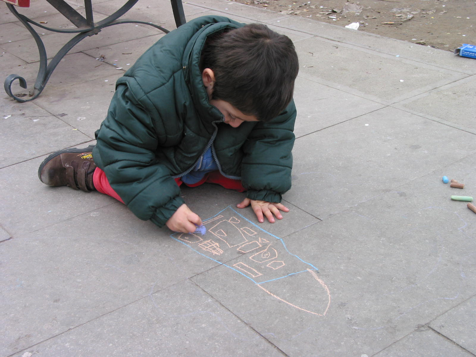 photo of a young boy drawing a building with chalk on the sidewalk