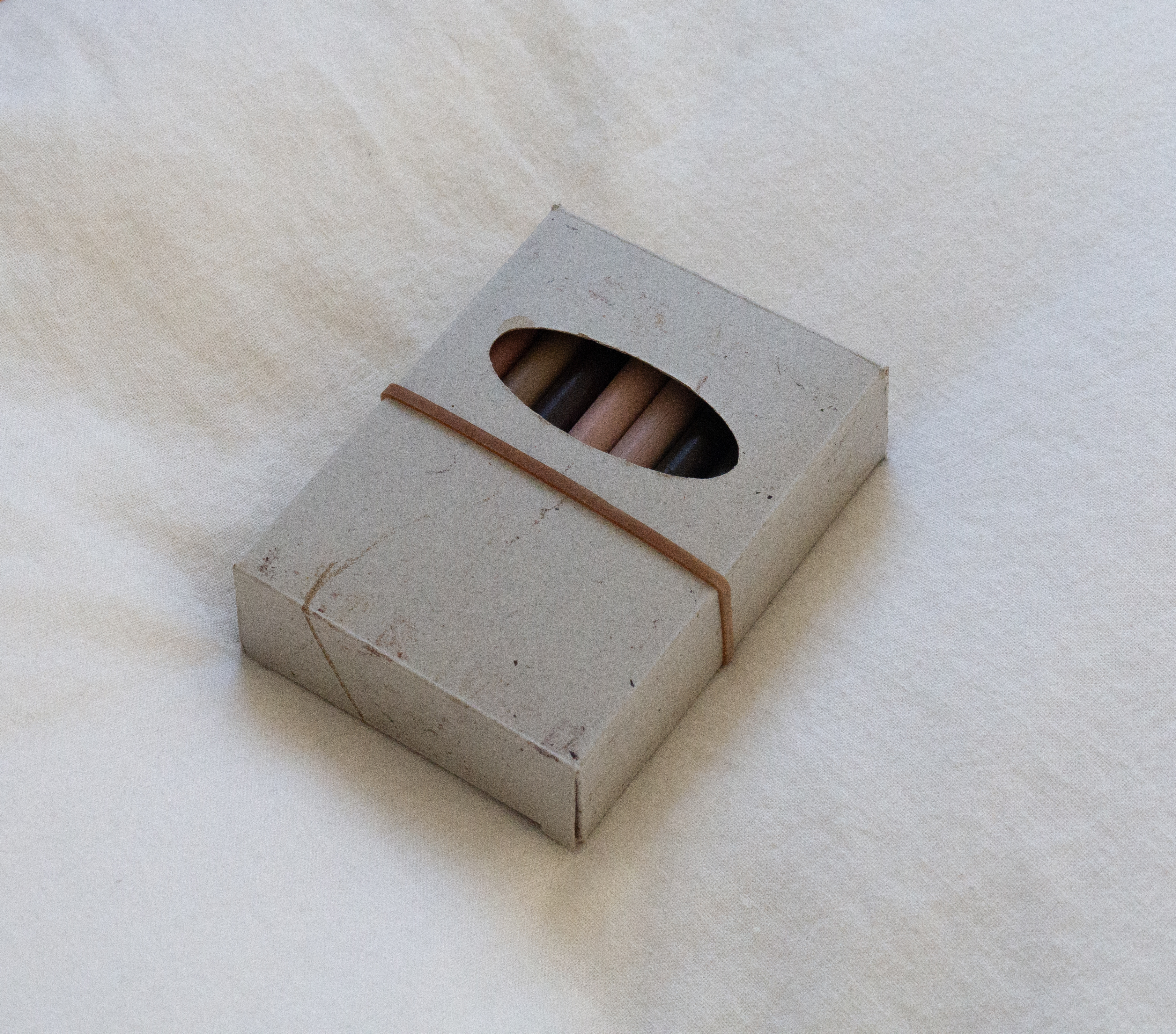 cardboard crayon box without branding, wrapped with a rubber-band, sitting on a white sheet
