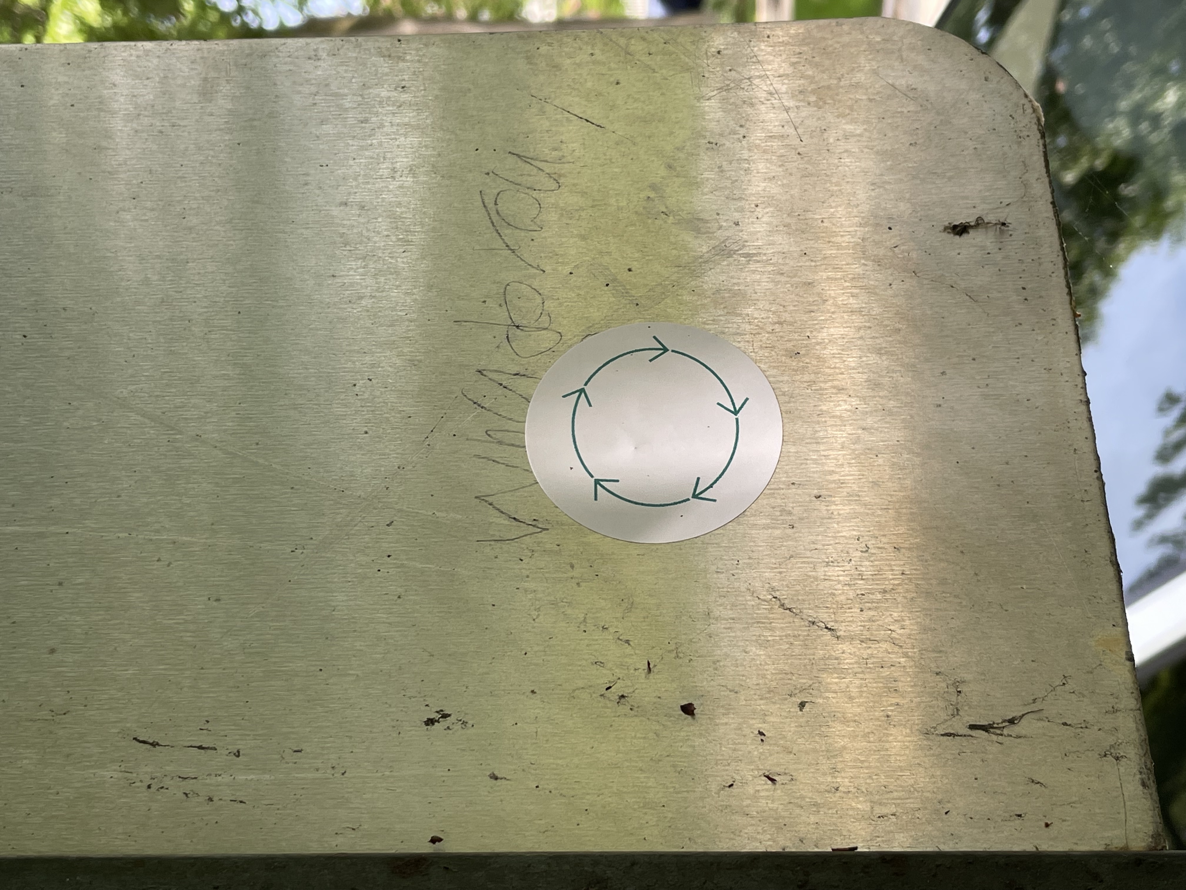 photo of a sticker on a street sign with a recycle logo of five green arrows