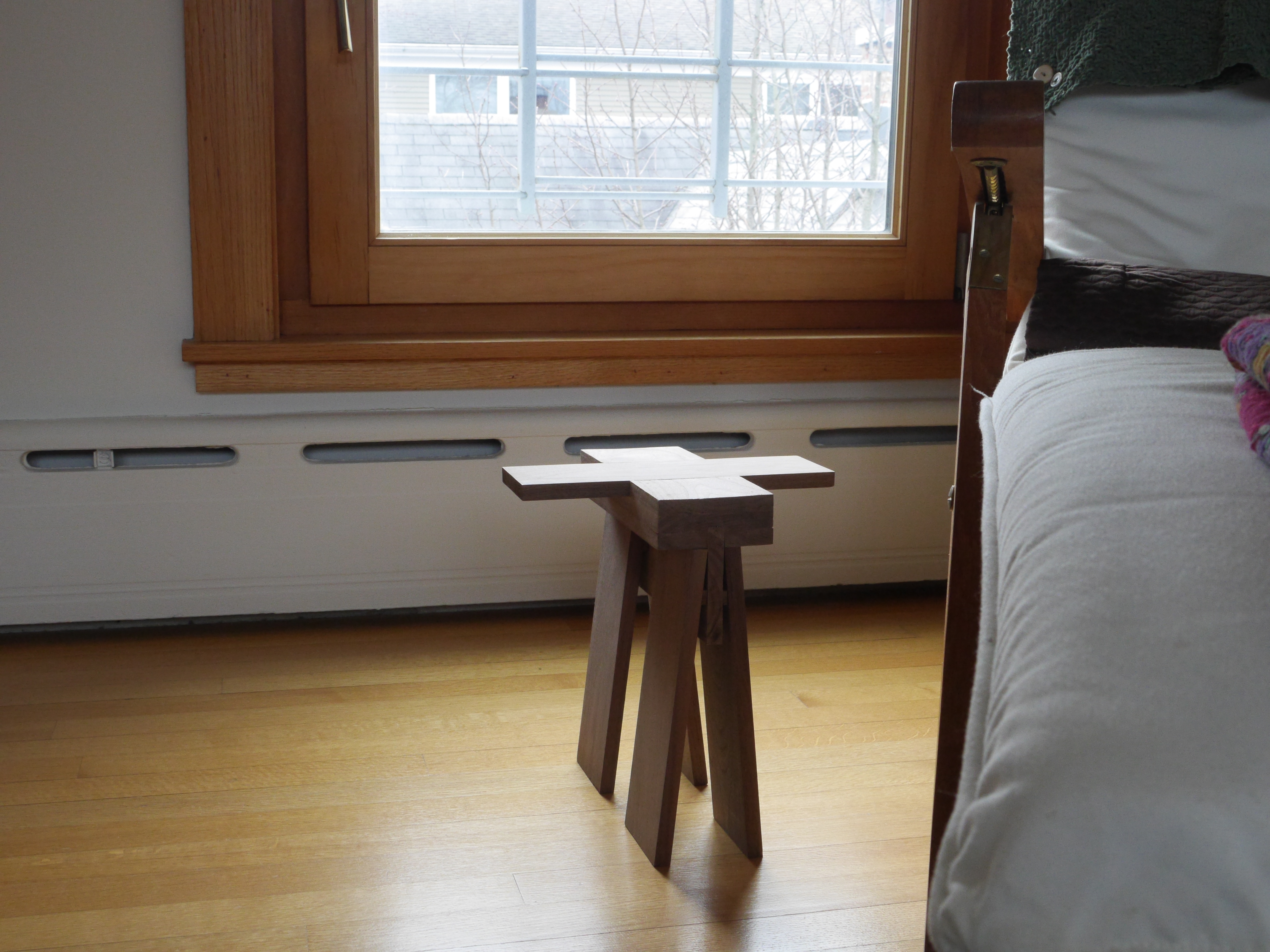 a wooden stool sits next to a lounge chair on a hardwood floor, and in the background is a window with wooden frame