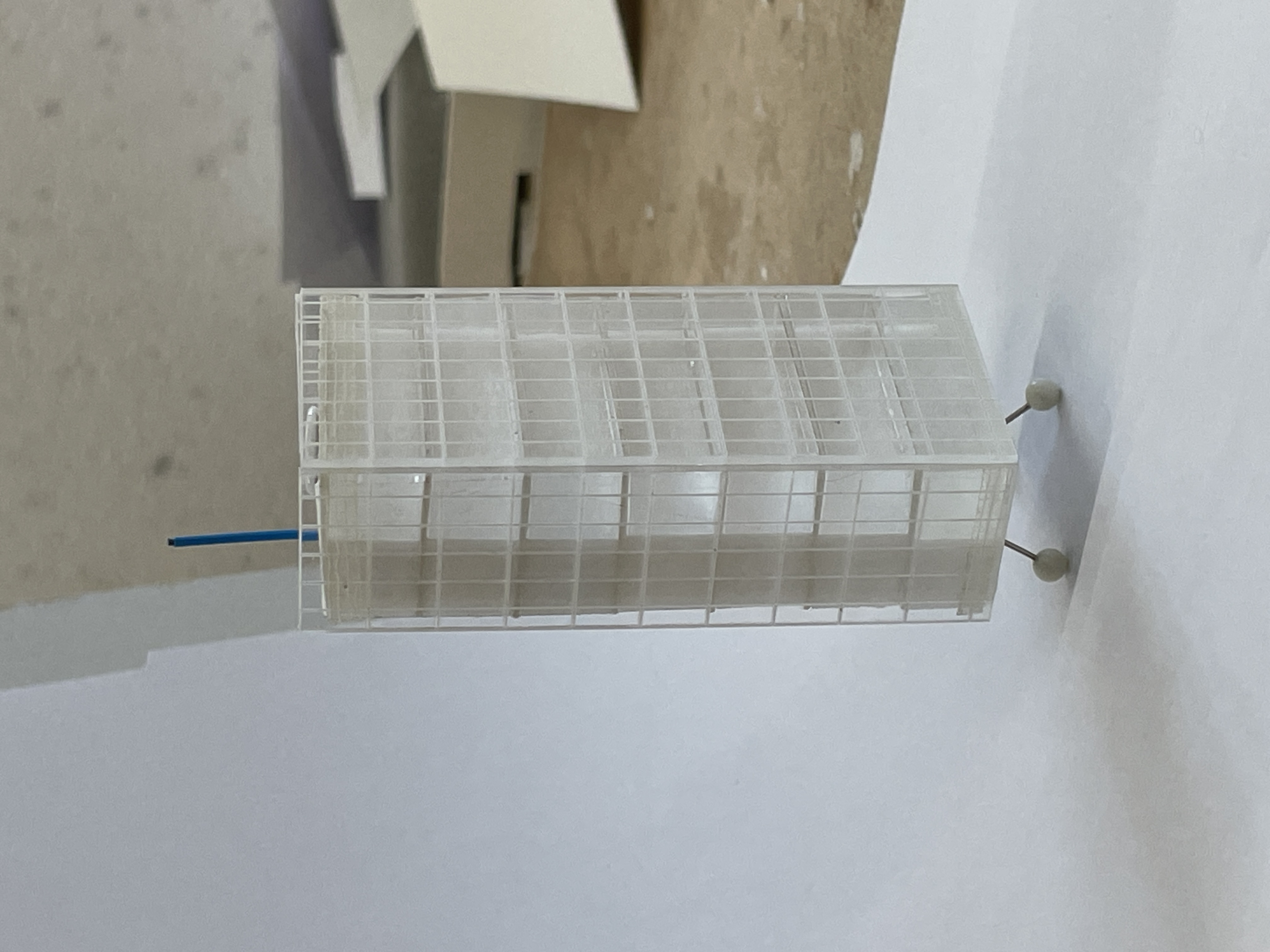 a small physical model of a tower sitting on three legs with a gridded facade and a small blue antenna coming from the roof